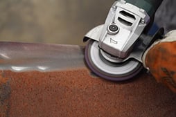 An operator uses a silicon carbide surface conditioning disc to remove rust for weld prep.